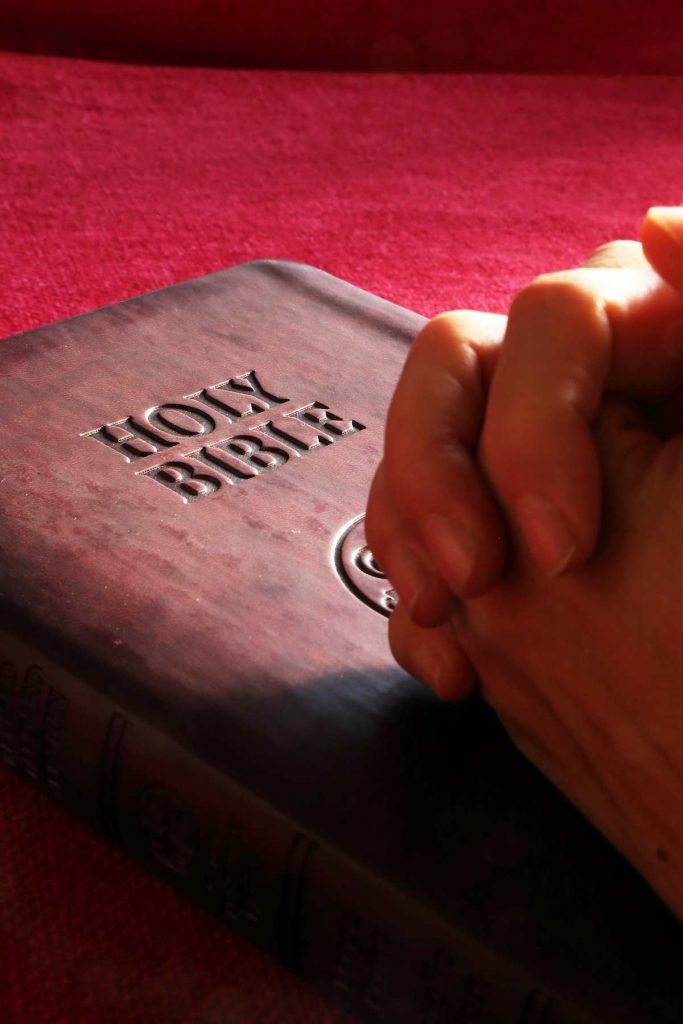 A woman clasps her hands in prayer over a bible.