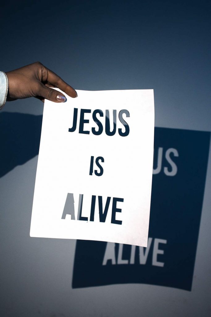 A girl holding a sign that says Jesus is alive.
